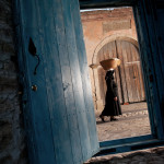an old lady walking on the stone paved street outside the blue front door in the old village center